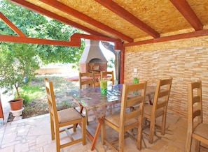 Relax in this charming outdoor space with a wooden table and four comfortable chairs, surrounded by a rustic brick wall and a shaded pergola.