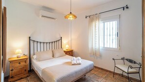 Un dormitorio con cama con dosel, mesitas de noche con lámparas, una ventana con cortinas y una silla.