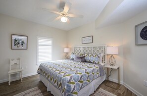 A bedroom with a bed, a ceiling fan, a bedside table with a lamp, a window with blinds, and a framed picture on the wall. - Luxury Beachfront 4BR/4BA Condo Sleeps 13 with Stunning Views and Large Balcony (Orange Beach)