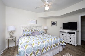 Une chambre à coucher avec un lit, un ventilateur de plafond, une télévision et un bureau.