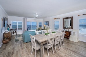 A spacious dining area with a wooden table and white chairs, a blue sofa, and a ceiling fan.