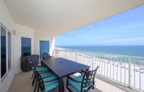 Ein Balkon mit Tisch und Stühlen, Blick auf den Ozean und ein Strand im Hintergrund.