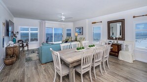 A spacious dining area with a wooden table and white chairs, a blue sofa, and a ceiling fan. - Luxury Beachfront 4BR/4BA Condo Sleeps 13 with Stunning Views and Large Balcony (Orange Beach)