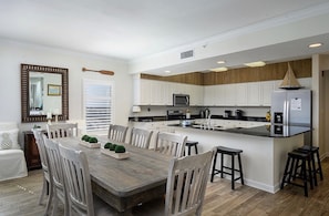 Une cuisine moderne avec des meubles blancs, une table à manger en bois et un îlot central intégré doté de tabourets de bar.
