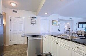 A kitchen with white cabinets, a stainless steel dishwasher, and a black countertop.