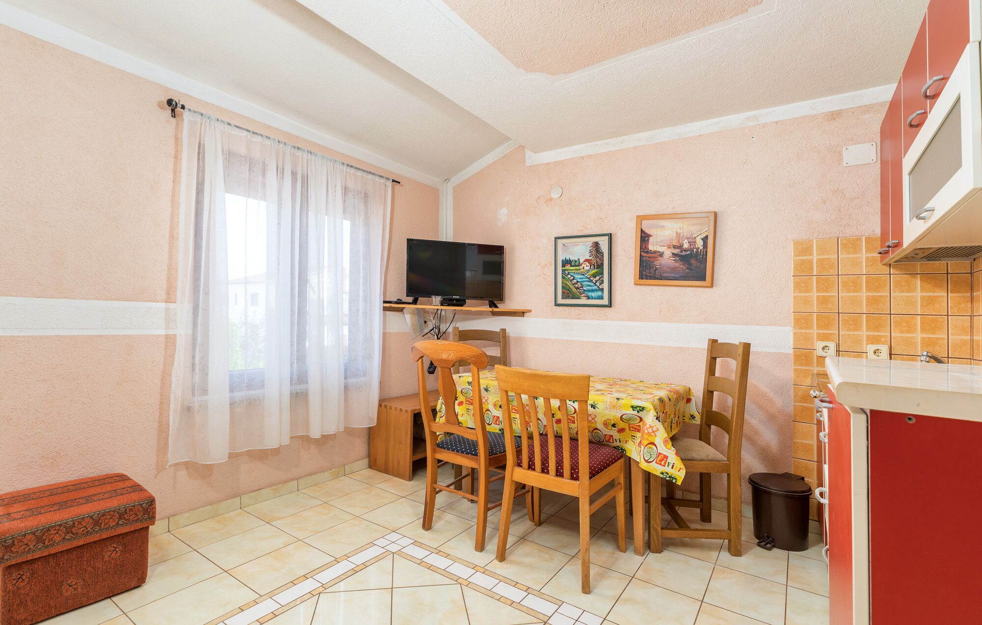 A compact kitchen with a dining area, a TV on a stand, and a painting on the wall.