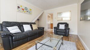 Un salon avec un canapé en cuir noir, une table basse en verre et un fauteuil en cuir noir. Un tableau est accroché au mur et un miroir se trouve au-dessus du fauteuil.