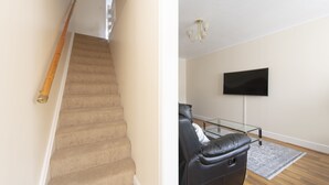 Un escalier avec une rampe en bois et un téléviseur fixé au mur dans un salon doté d’un canapé en cuir et d’un tapis à motifs.