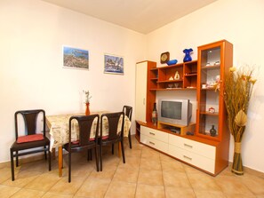 Ein Essbereich mit Tisch und Stühlen, einem Fernseher auf einer Holzkommode und zwei gerahmten Bildern an der Wand.