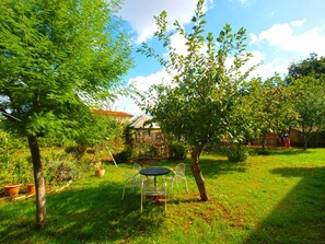 Ein Garten mit Tisch und Stühlen, umgeben von Bäumen und Topfpflanzen.