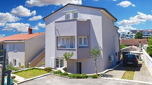 A two-story residential building with a sloped roof, a small front garden, and a parked car in the driveway.