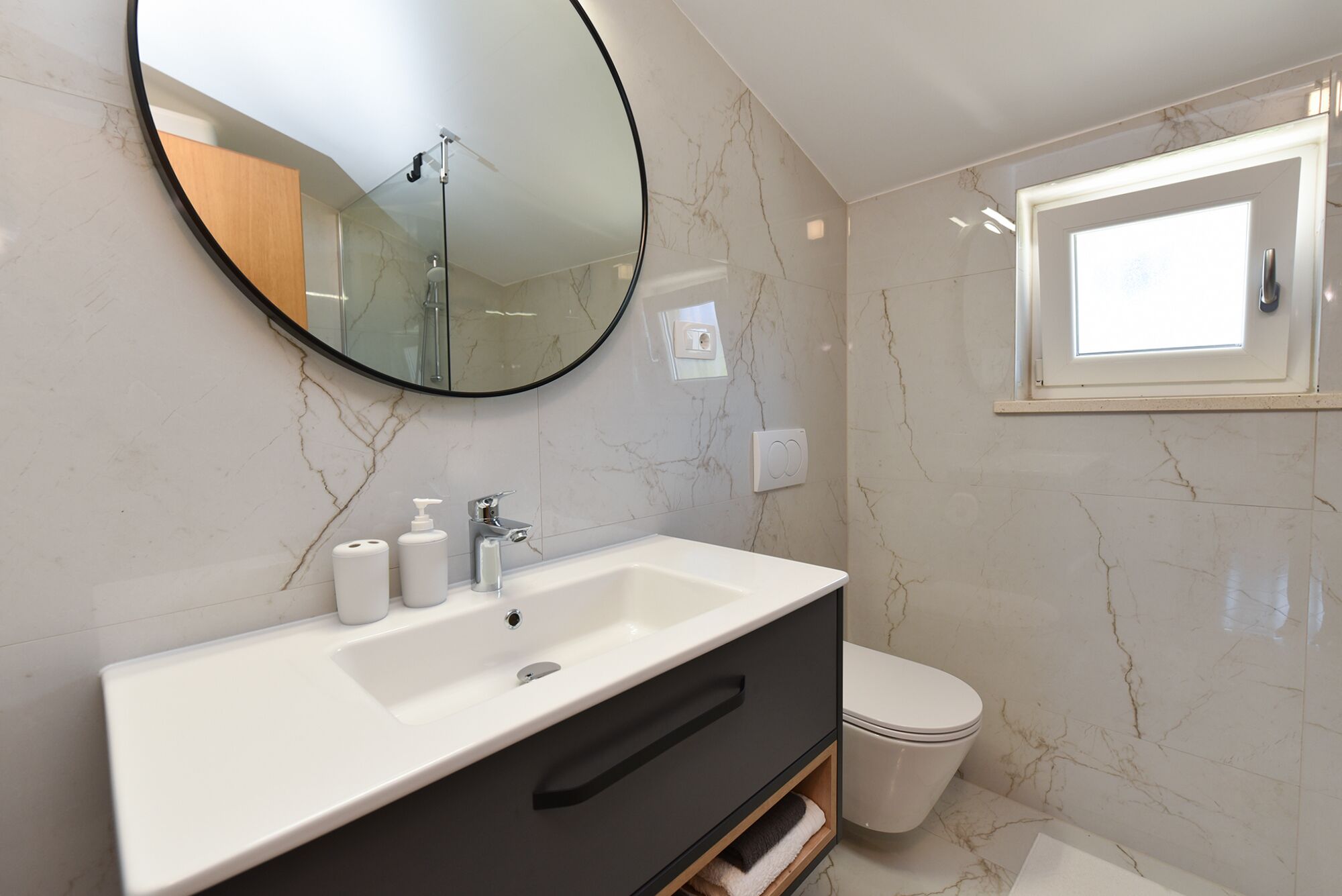 A bathroom with a white sink, a mirror, a toilet, and a window.