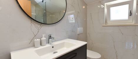 A bathroom with a white sink, a mirror, a toilet, and a window.