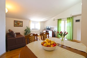 Una sala de estar con un sofá, sillas, una mesa de comedor con fruteros, un televisor y una ventana con cortinas.