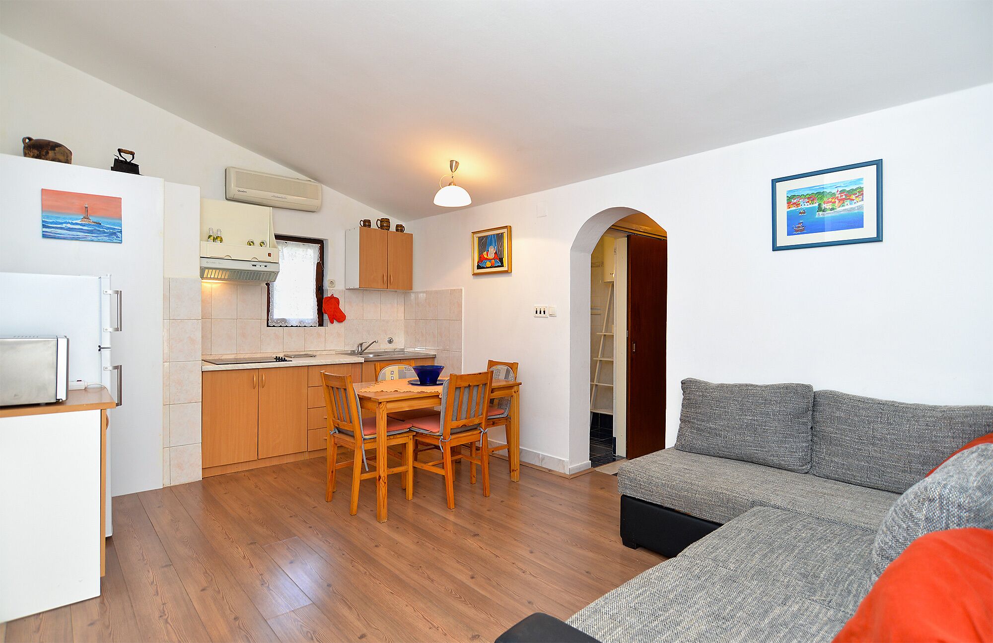 A compact living space with a kitchenette, a dining area with a table and chairs, and a grey sofa.
