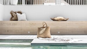 Un área de piscina con un bolso tejido y una almohada blanca sobre un repisa de madera.