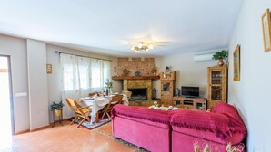 A cozy living room with a fireplace, a dining area with a table set for two, and a television in a wooden cabinet.