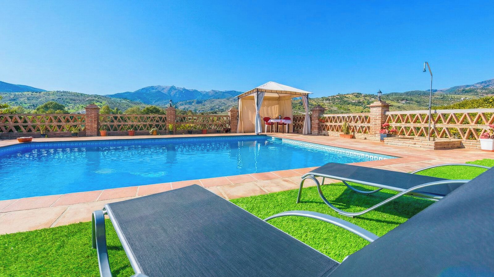 A swimming pool with lounge chairs, a covered seating area, and a view of mountains.