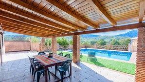 A covered patio with a pool, outdoor seating, and a view of the mountains.
