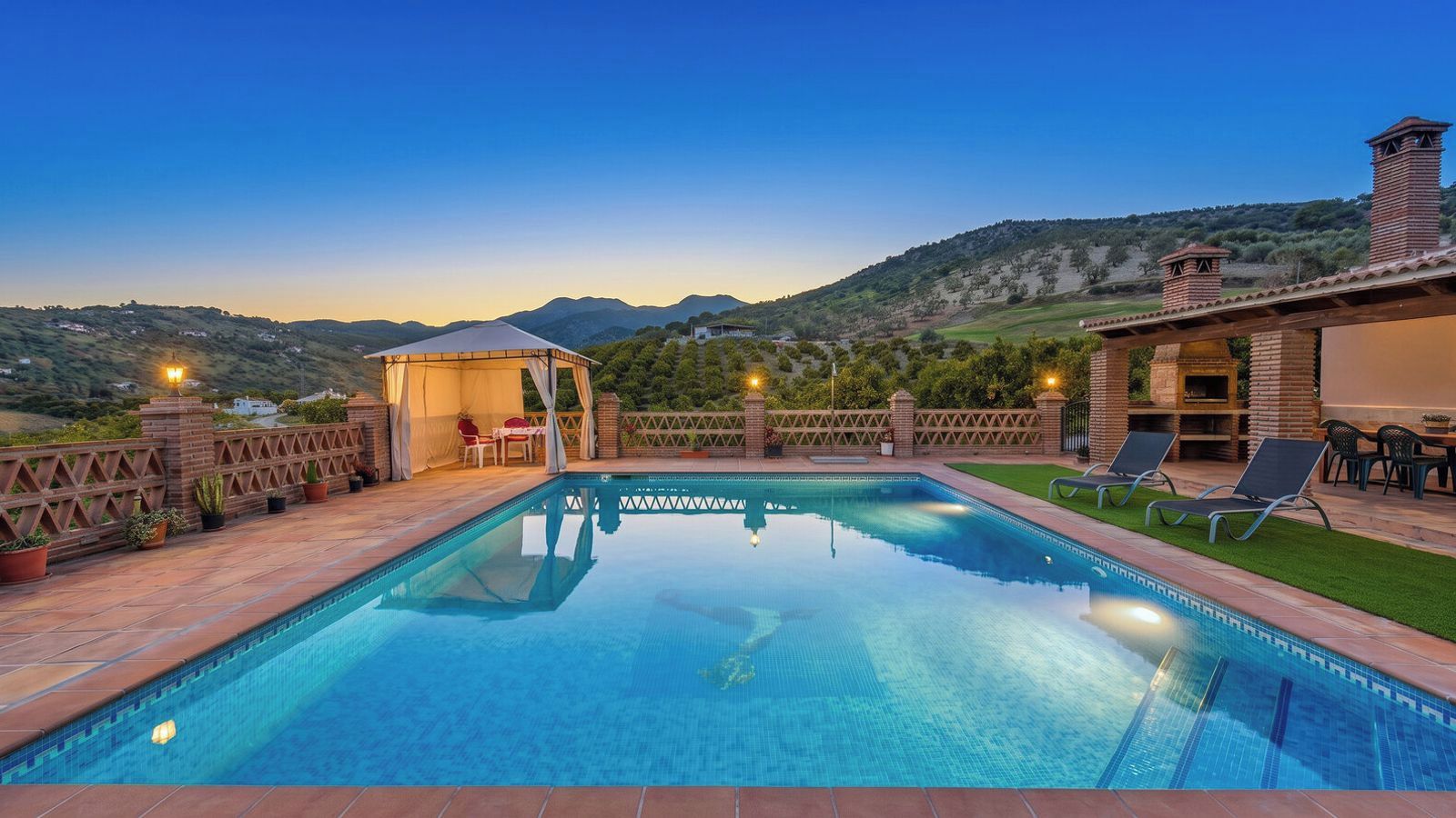 A swimming pool with a view of mountains, a covered seating area, and outdoor furniture.