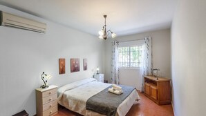 A bedroom with a bed, bedside table, lamp, wall art, window with curtains, and a wooden dresser.