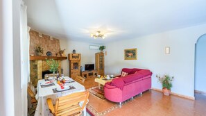 A living room with a fireplace, a dining area with a table set for two, and a red sofa. - Río Grande de Tolox by Ruralidays (Málaga)