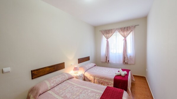 A bedroom with two beds, a nightstand with a lamp, and a window with curtains. - Río Grande de Tolox by Ruralidays (Málaga)