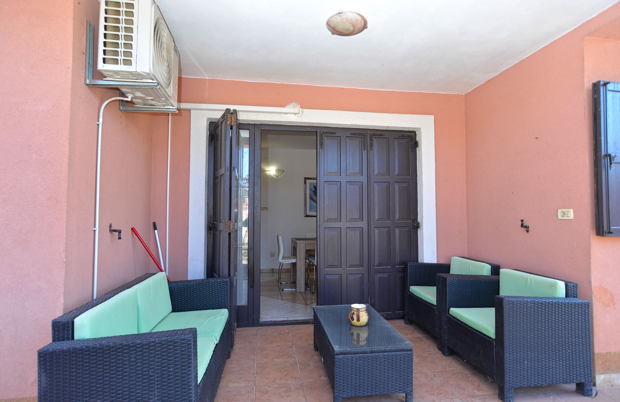 An outdoor seating area with wicker furniture and a table, a sliding glass door leading to an interior space, and an air conditioning unit mounted on the wall.