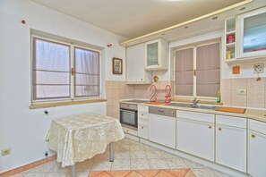 A kitchen with white cabinets, a double sink, a dishwasher, and a table with a lace tablecloth.