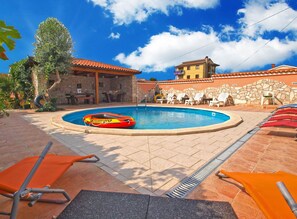 A swimming pool with lounge chairs, a stone wall, and a building with a tiled roof.