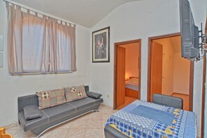 A bedroom with a bed, a sofa, a television, and a door leading to another room.