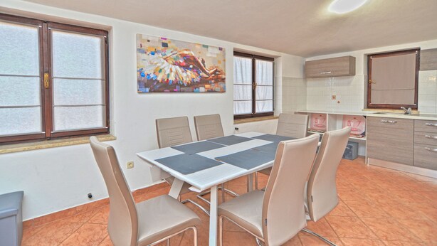 Uma área de refeições com mesa e cadeiras, um quadro na parede e uma cozinha com armários e uma janela.
