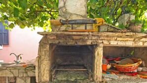 Forno rústico ao ar livre construído em pedra, com interior de tijolo, rodeado por paredes de pedra e bancada de pedra.