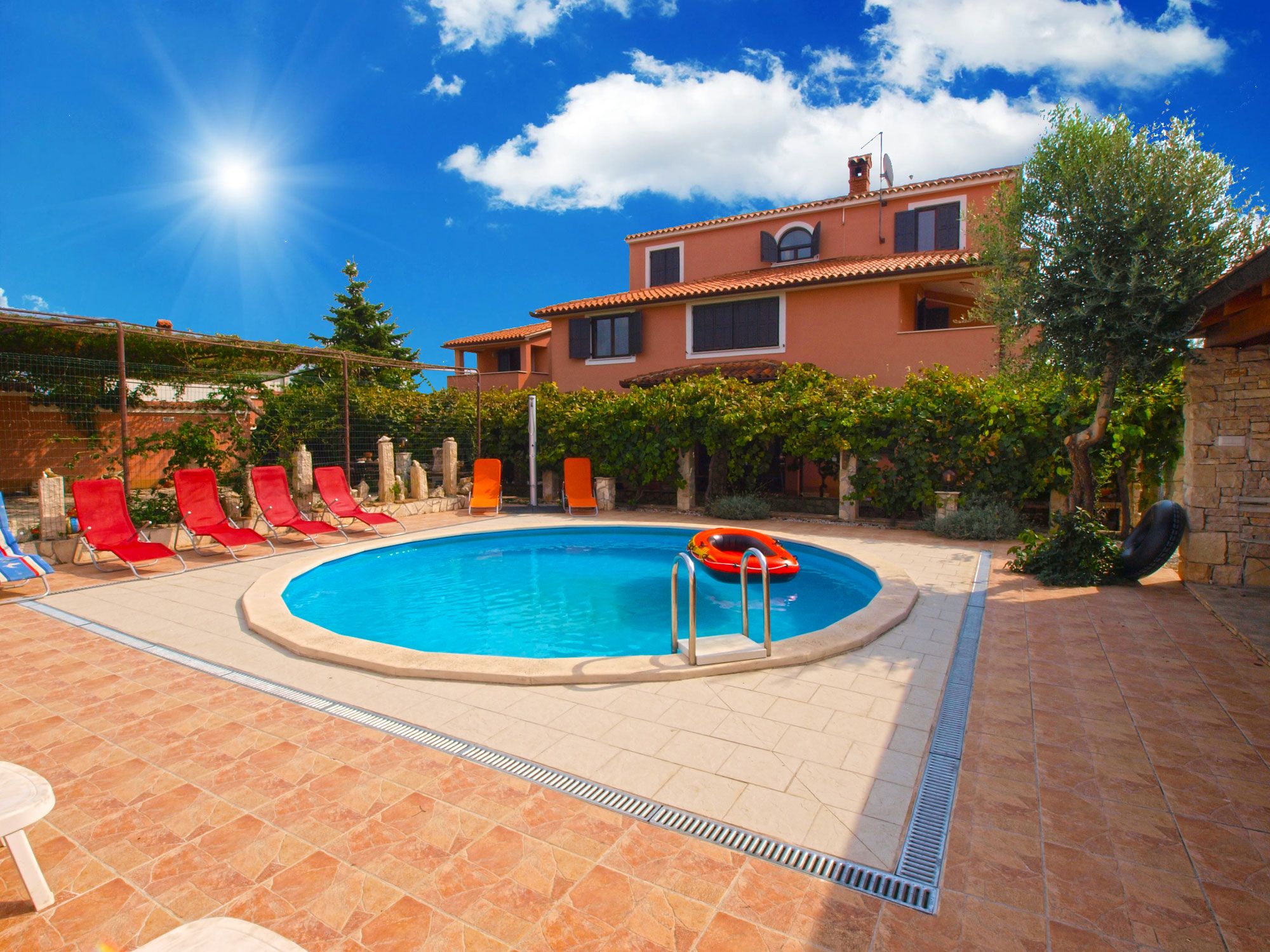 A swimming pool with red lounge chairs, a lifebuoy, and a stone building in the background.