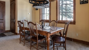 Zona pranzo con tavolo e sedie in legno, un lampadario e una finestra vista alberi.