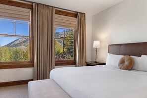 A hotel room with a large bed, a nightstand, a lamp, and a view of a mountain landscape through the window.