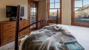 Una camera da letto con un letto, una cassettiera, una televisione e una finestra vista montagna.