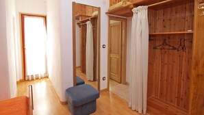 Une chambre avec une armoire en bois, un lit, un banc et un miroir.