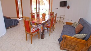 Un coin repas avec une table et des chaises, un canapé, un téléviseur et une fenêtre avec des rideaux.