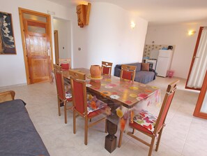 A dining area with a wooden table and chairs, a kitchen in the background, and a door leading to another room.