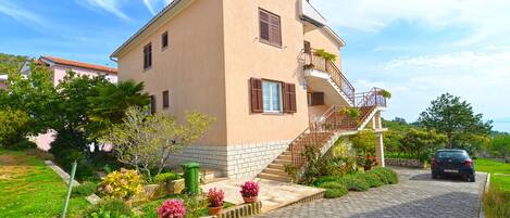 A two-story house with a stone foundation, a balcony with a metal railing, and a paved driveway.