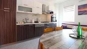 A modern kitchen with dark wooden cabinets, a white countertop, and a dining area with a wooden table and chairs. - Apartment 768/1789 (Istria - Fažana), 500m from the beach (Fažana)