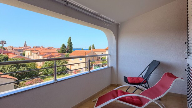 A balcony with two red lounge chairs, a view of a coastal town, and a tiled floor. - Apartment 771/1799 (Istria - Fažana), 300m from the beach (Fažana)