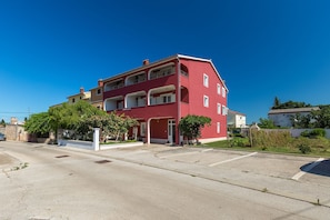 Un immeuble résidentiel rouge à plusieurs étages, doté de balcons, d’une allée et entouré de verdure.