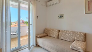 A room with a sliding glass door leading to an outdoor area, a beige sofa with floral cushions, a wall-mounted air conditioner, and a framed picture on the wall. - Apartment 771/1800 (Istria - Fažana), 300m from the beach (Fažana)