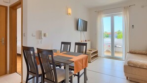 A dining area with a table and chairs, a TV mounted on the wall, and a sliding glass door leading to an outdoor balcony. - Apartment 771/1800 (Istria - Fažana), 300m from the beach (Fažana)