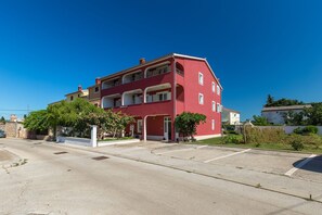 A red multi-story residential building with balconies, a driveway, and surrounding greenery.