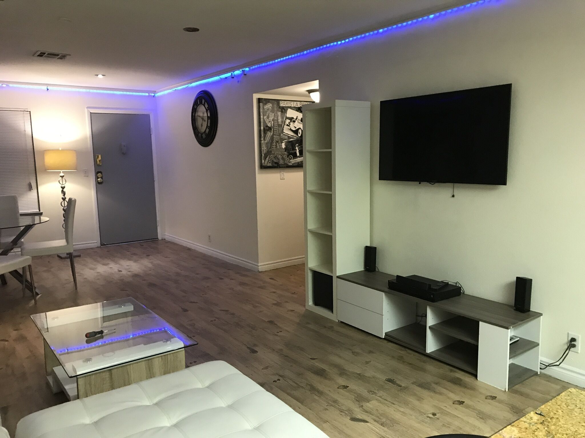Un salon moderne doté d’un téléviseur à écran plat, d’une horloge et d’un coin repas avec une table et des chaises.