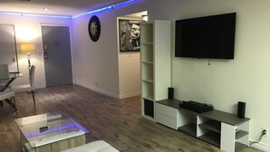 A modern living room with a flat-screen TV, a clock, and a dining area with a table and chairs. - La Cassita Beautiful Condo WOW!!!! (Las Vegas)