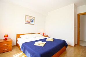 A hotel room with a bed, two bedside tables, a nightstand, a painting on the wall, and a door.